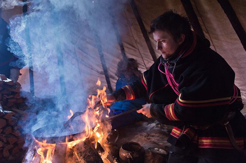 A man in traditional Sami clothing cooking over a fire.