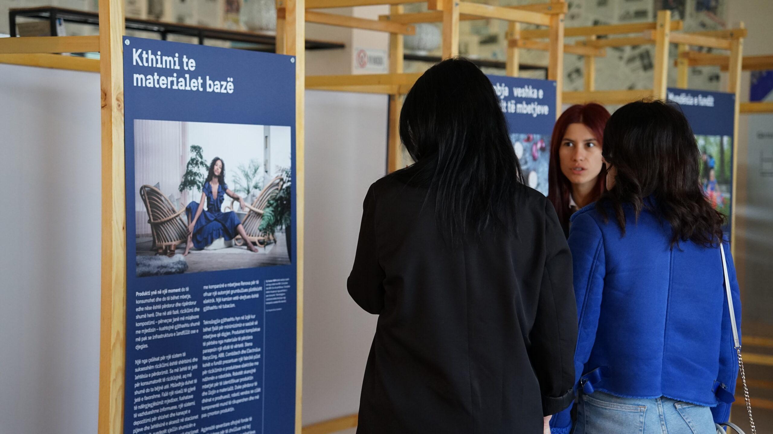 Three women looking at a poster on recycled fashion.