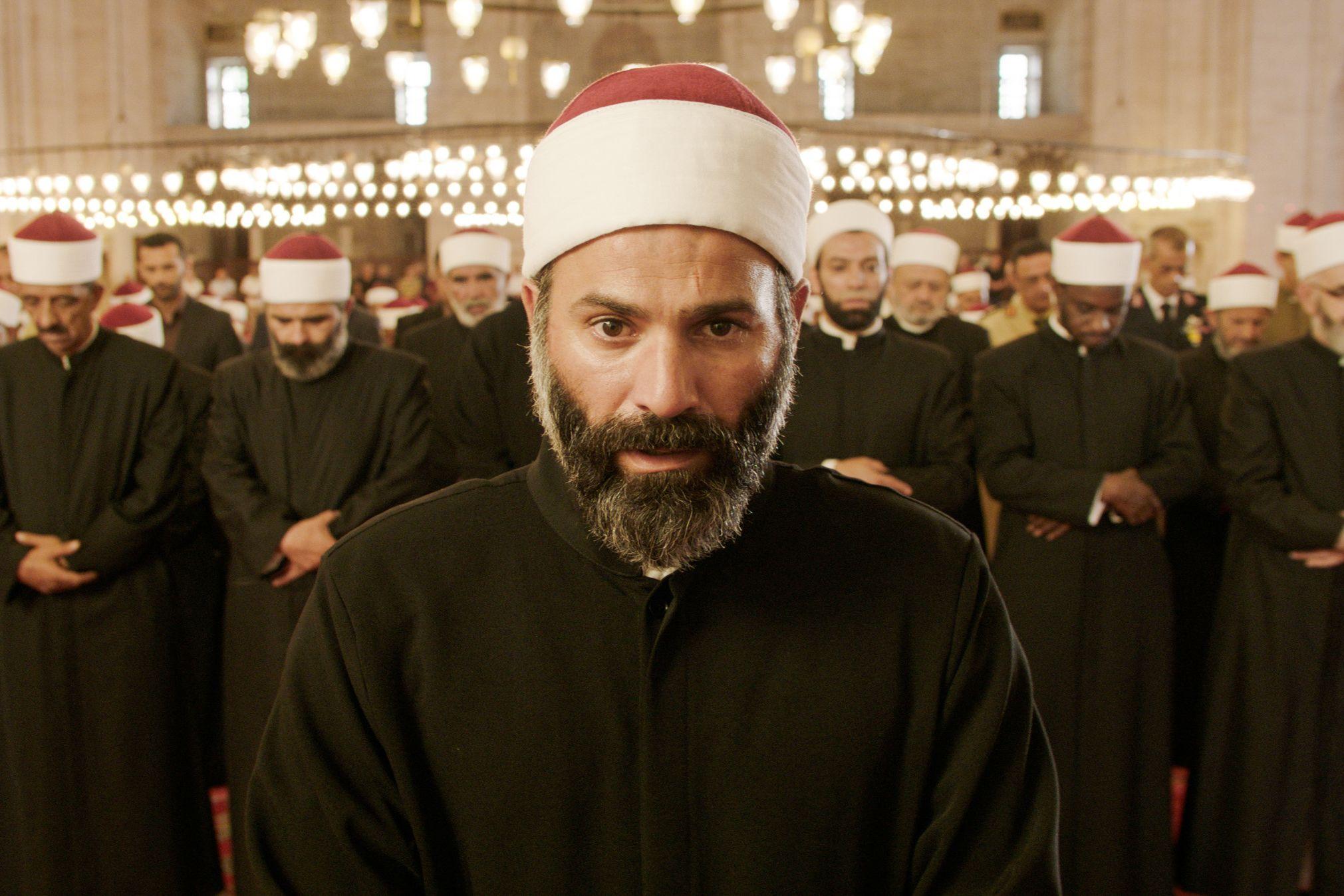 A man looking emotional with other men praying behind him. 