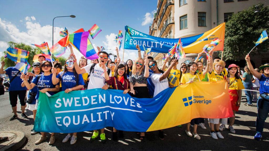 People at a pride parade with a Sweden banner.