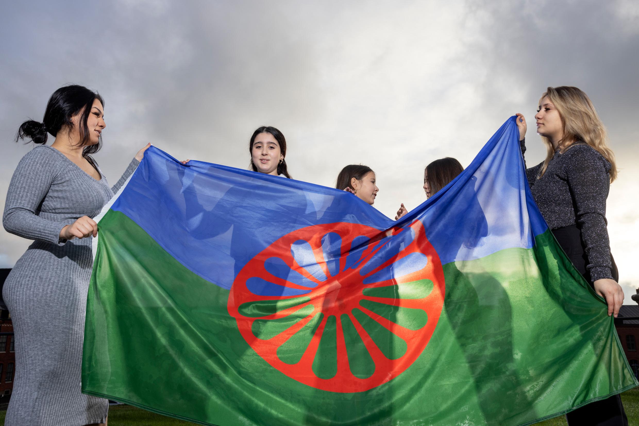 Young women holding the blue, green and red Roma flag.