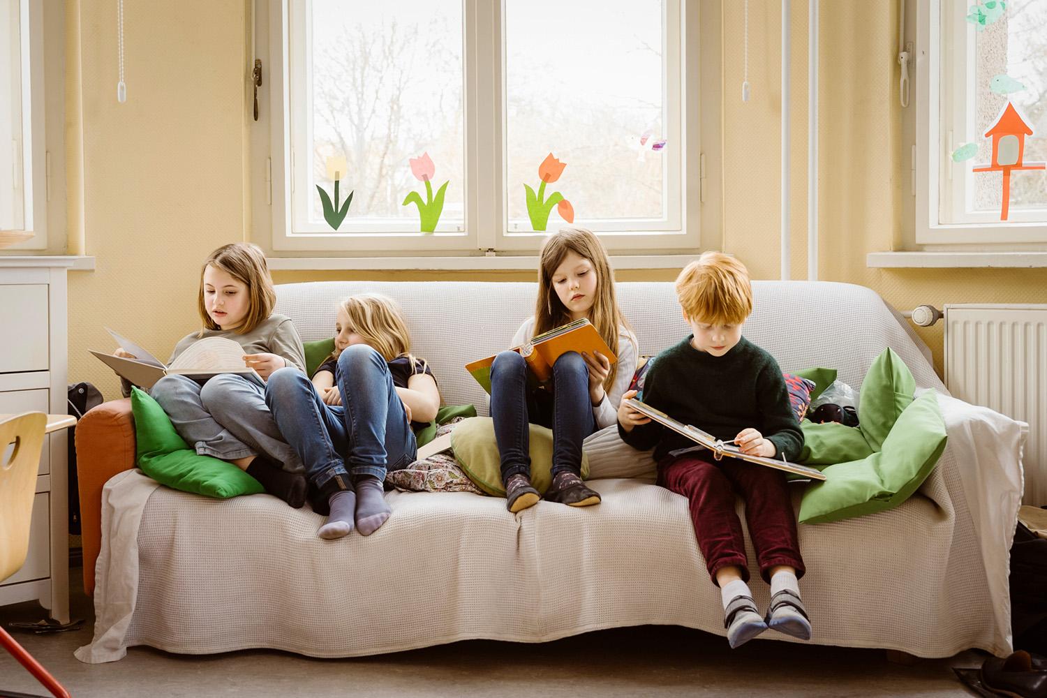 Children reading books together on a sofa.