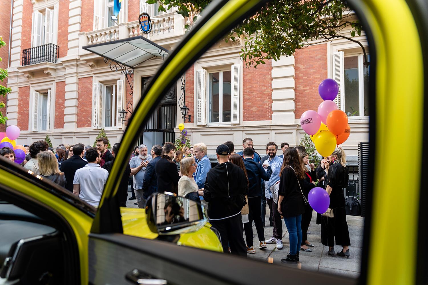 People with balloons in front of the embassy, viewed through a car door. 