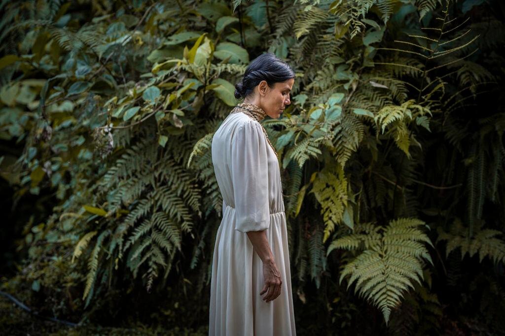 A woman in a white dress standing in front of the jungle.