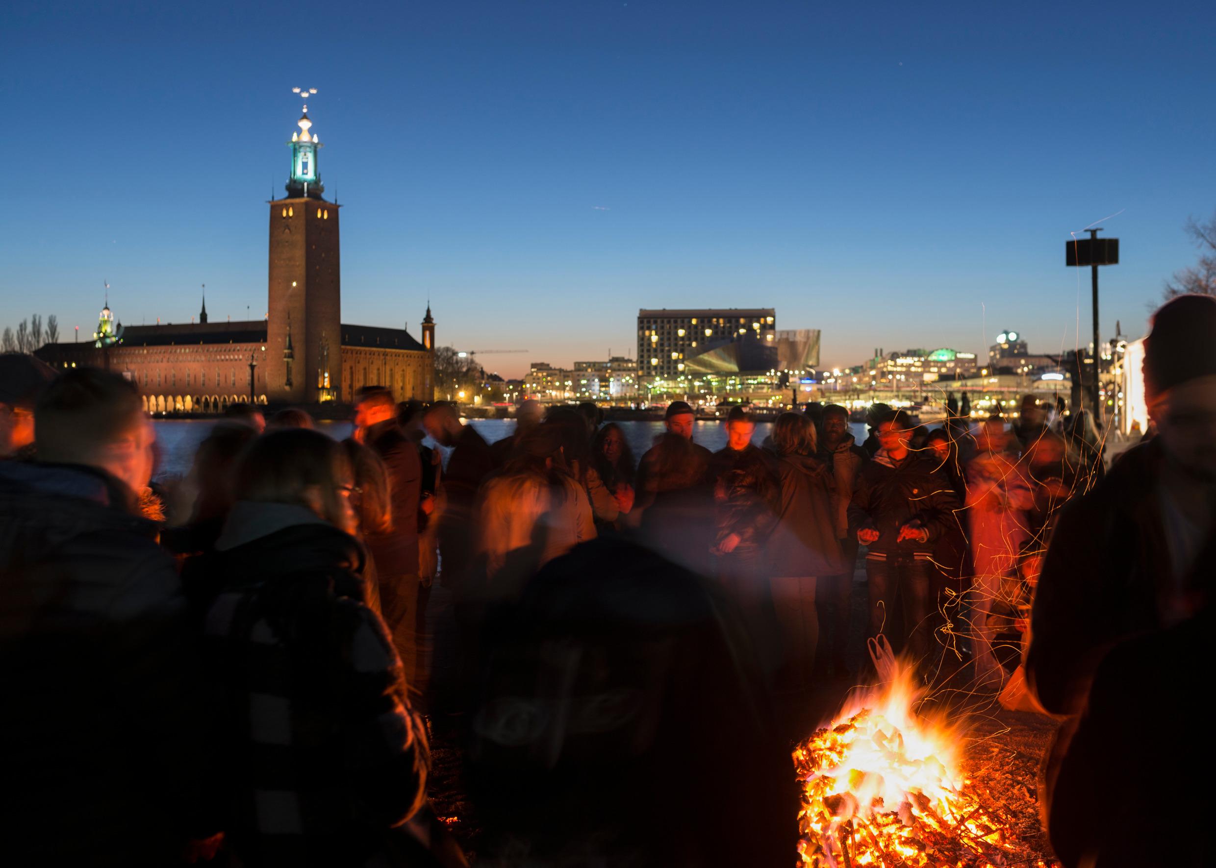 Crowds of people stand in the dark looking at a bonfire.