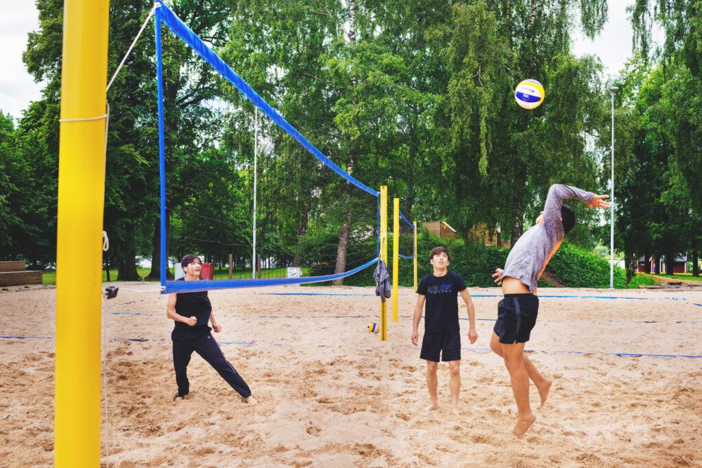 Three persons playing beach volley ball with green trees in the background.