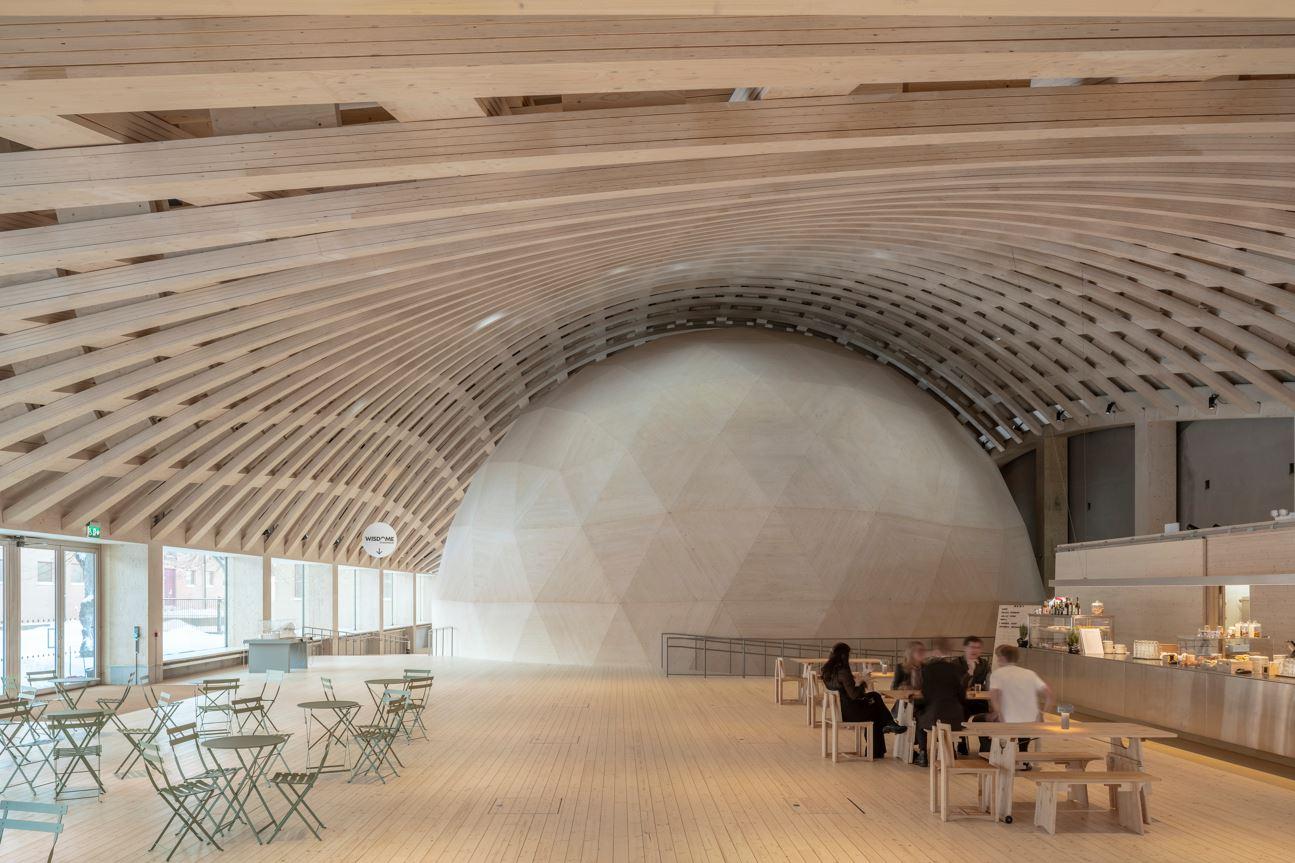 A café inside Wisdome Stockholm with walls in wood and a large wood dome. 