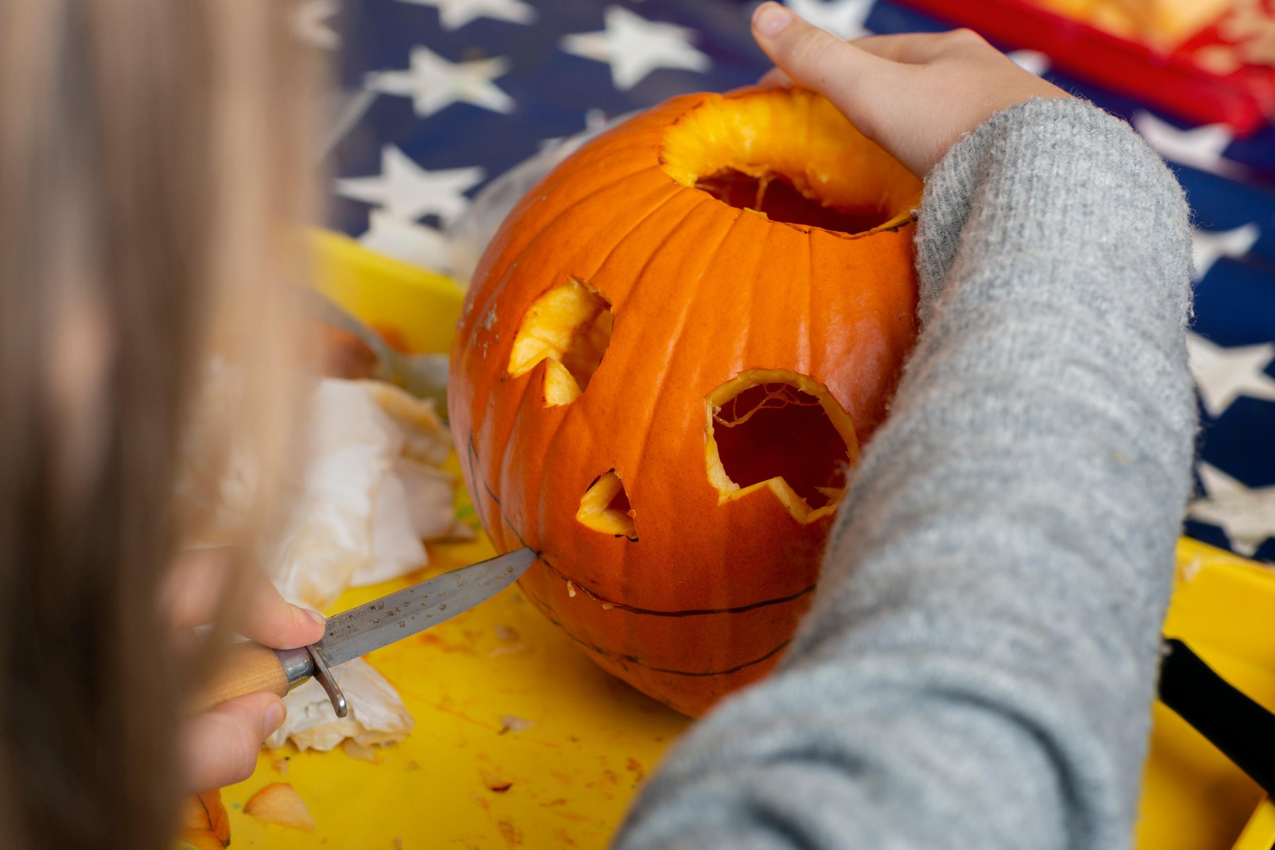 A kid is carving a pumpkin with a knife.