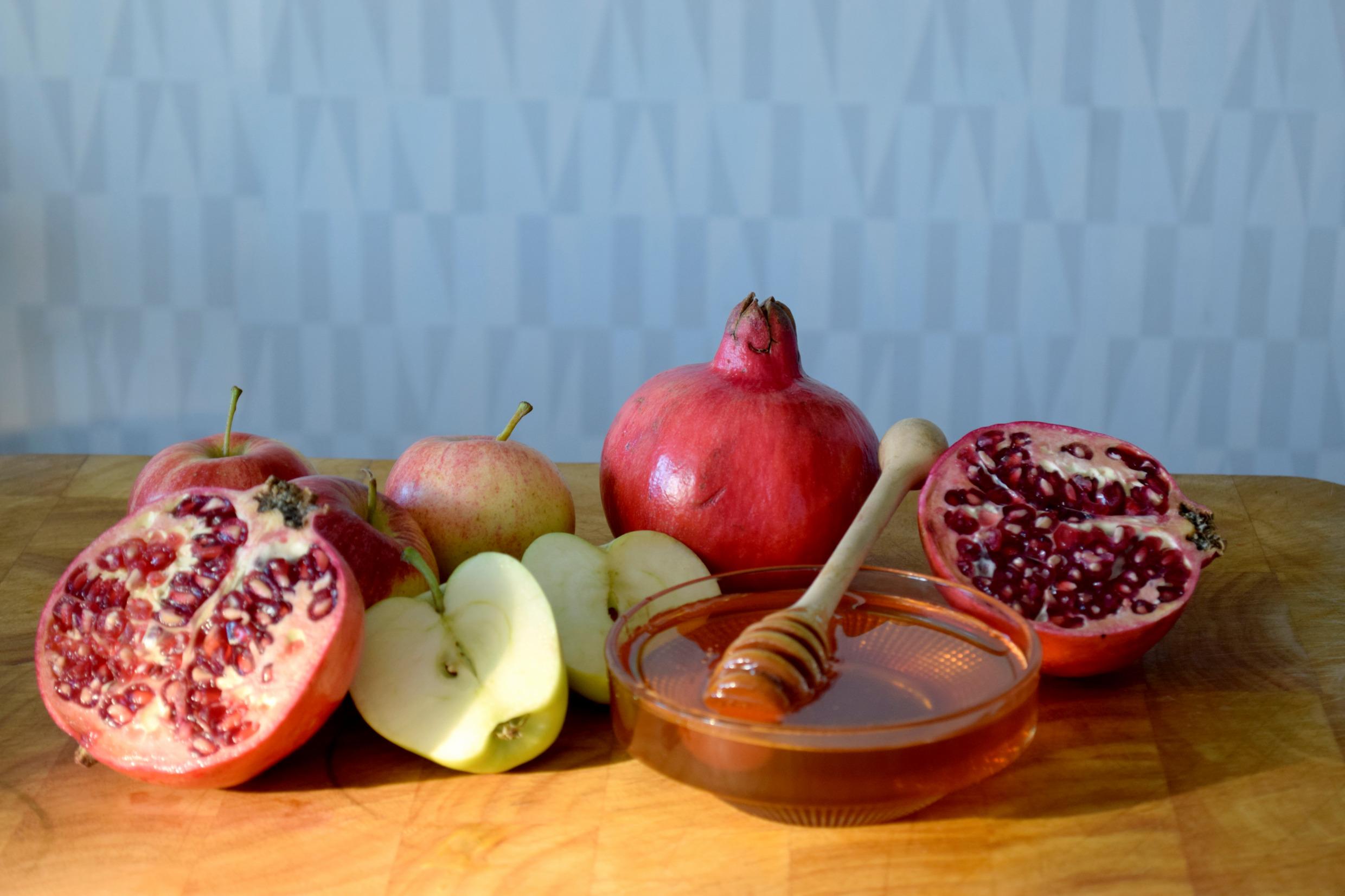 Apples, pomegranates, and honey in a bowl are arranged on a table.