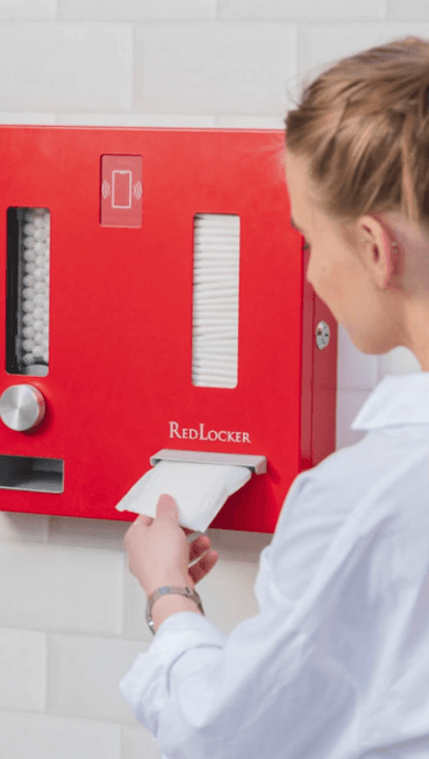 A girl taking a free pad from a red locker.