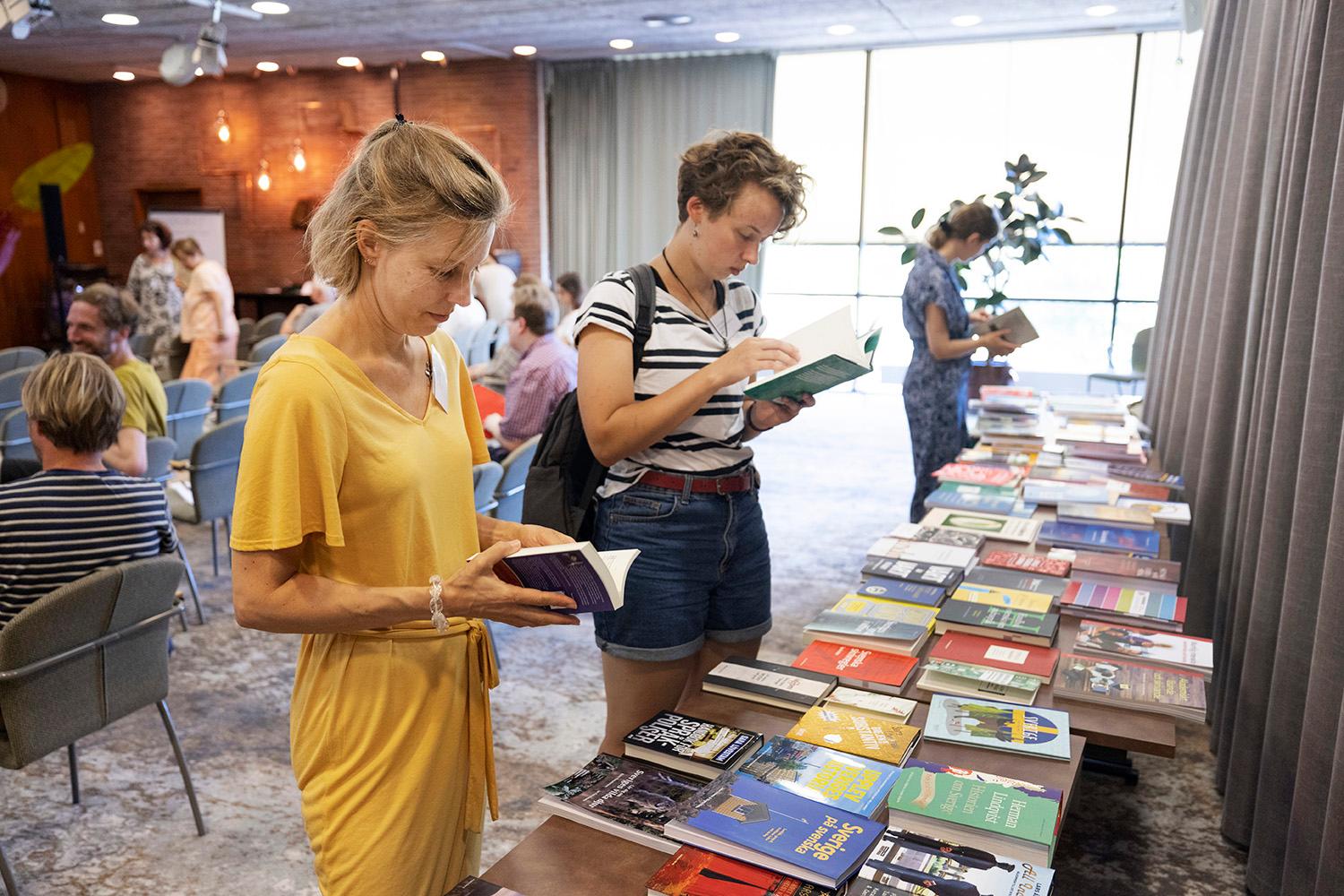 People reading Swedish books, one in a yellow dress and the other in blue shorts and a striped t-shirt.