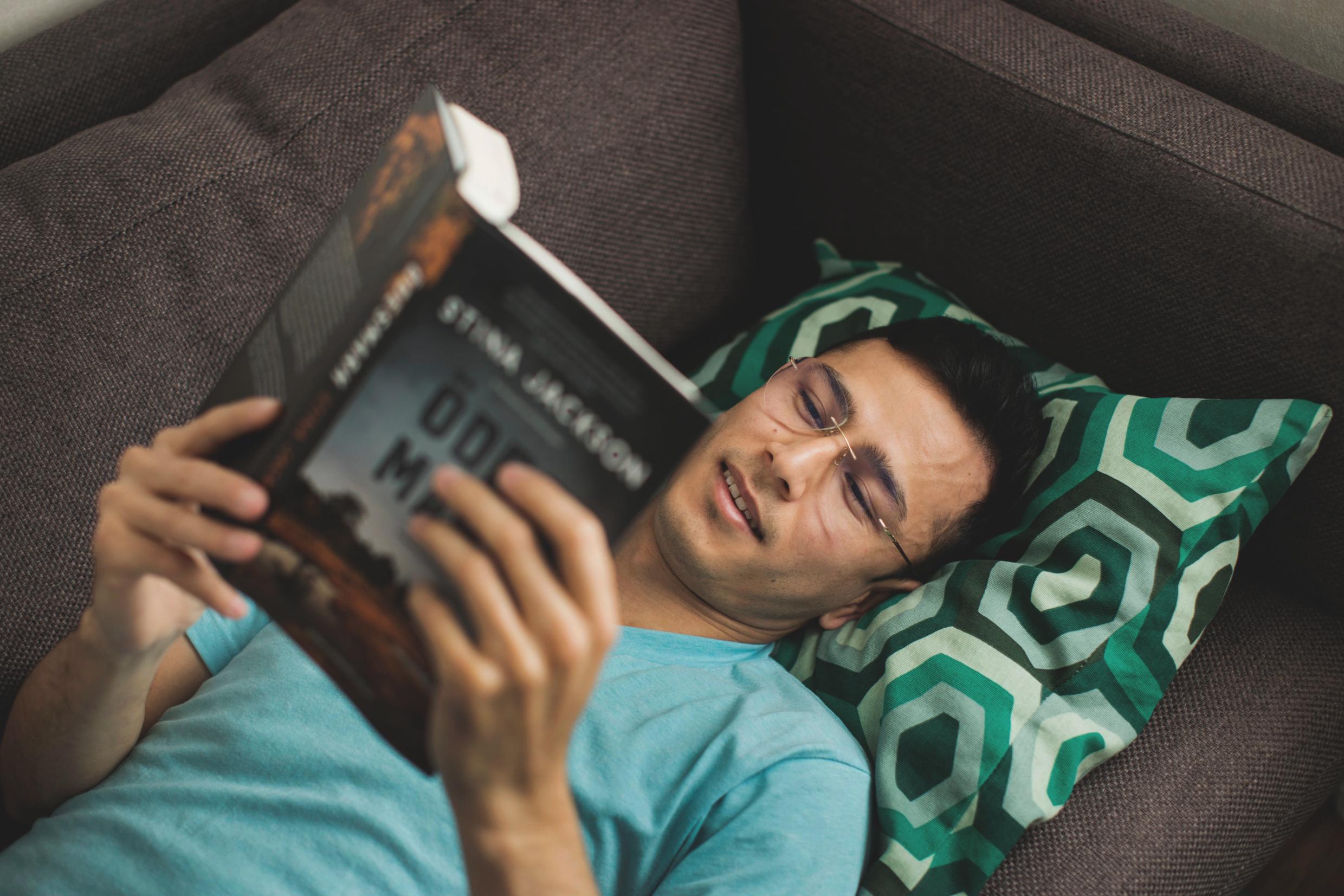 A man lies in a sofa, holding a book.