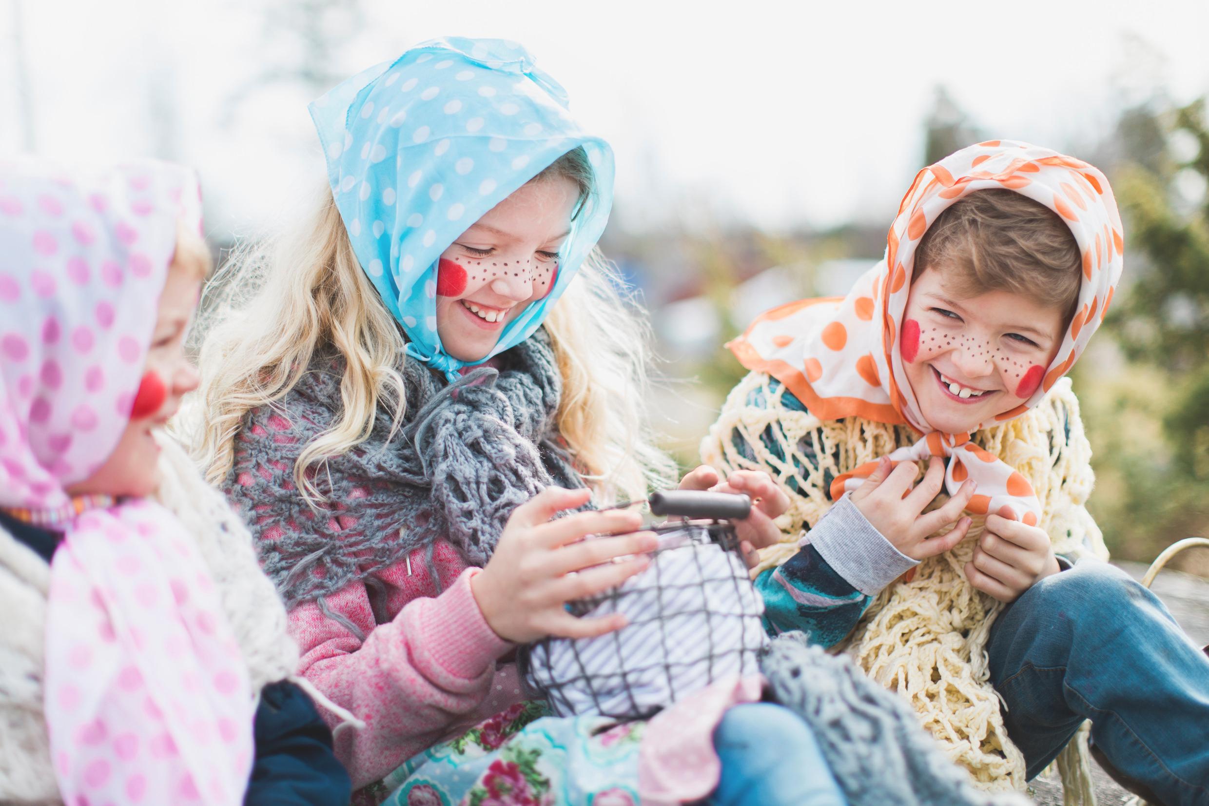 Three laughing girls are dressed up as Easter witches with colourful clothes and headscarf.
