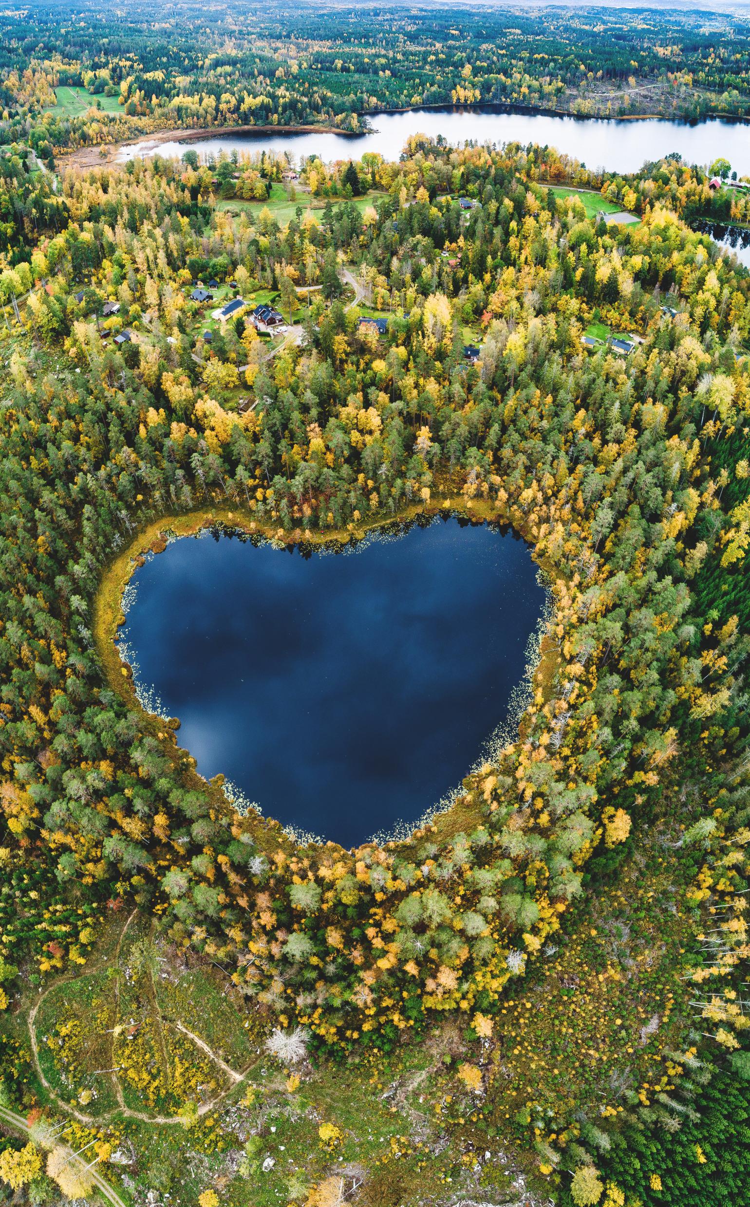 Drone image of a heart-shaped lake. Around the lake are trees in autumn colours.