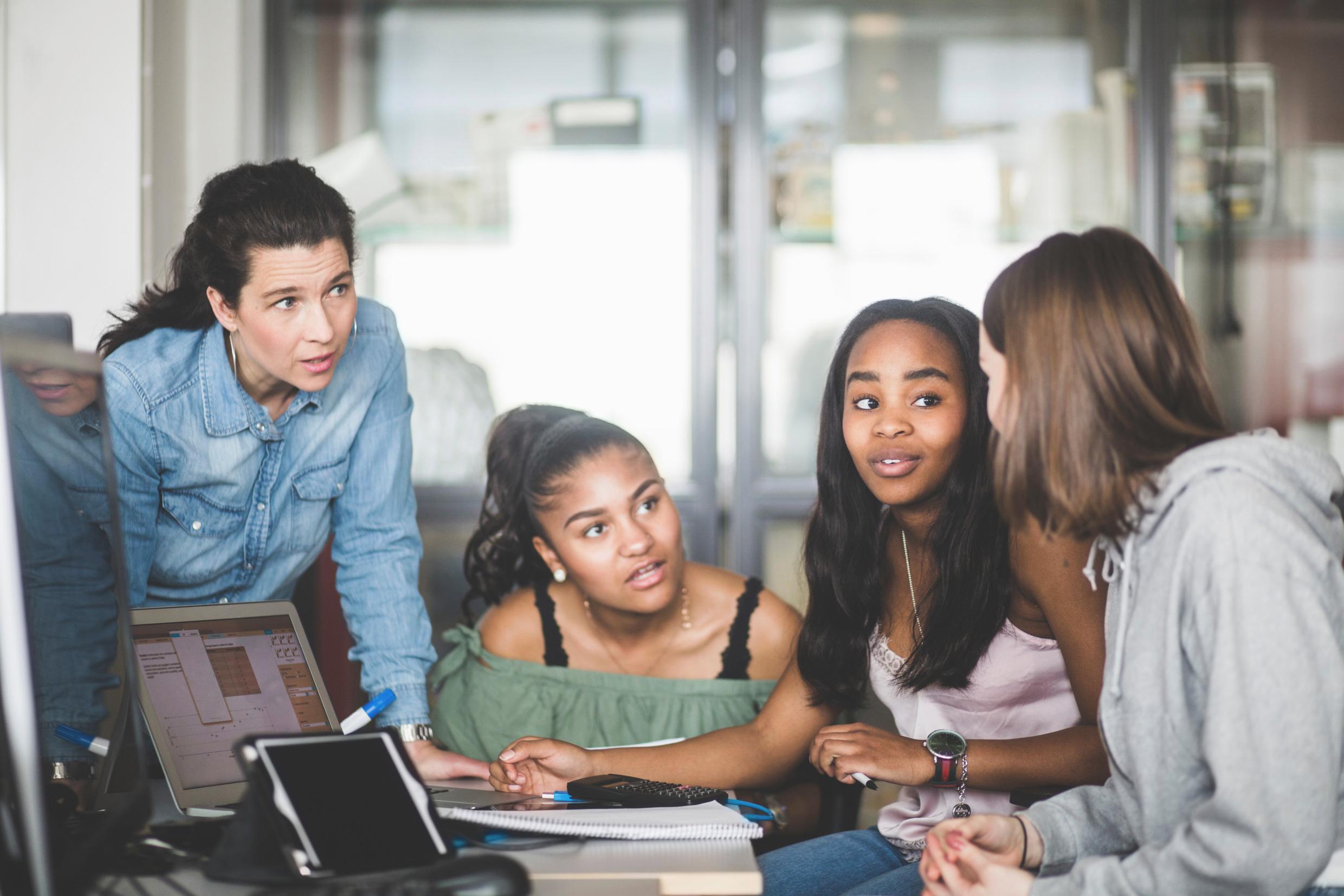 A female teacher helping three teenage girls.