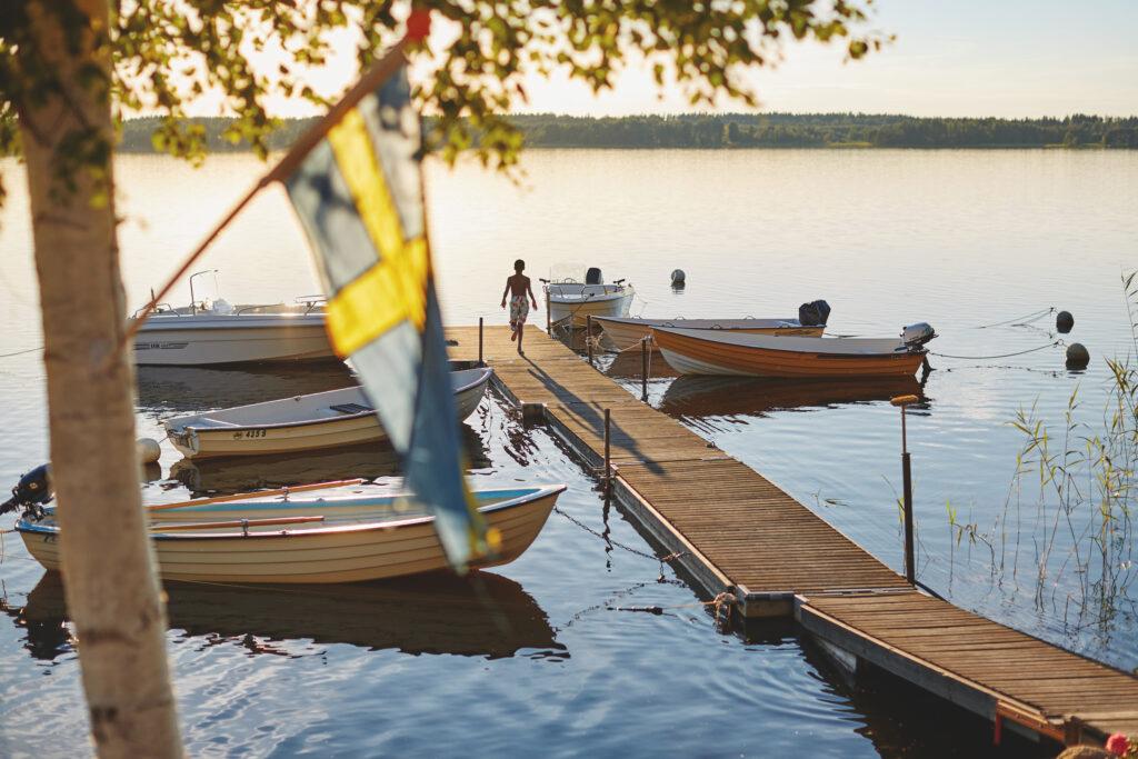 A boy runs down a wooden pier that has small boats moored to it.
