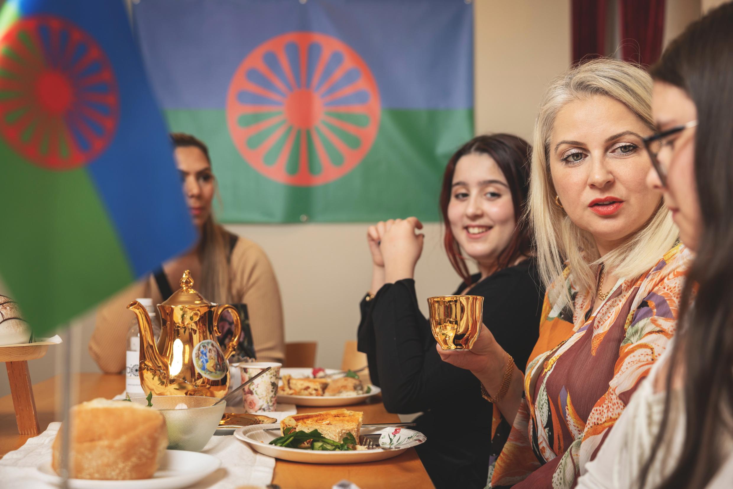 Women drinking tea and Roma flags on the wall.
