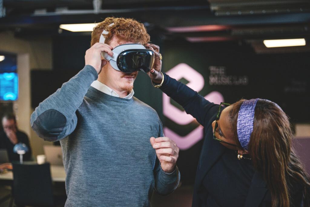 A woman helping a man adjust a VR headset.