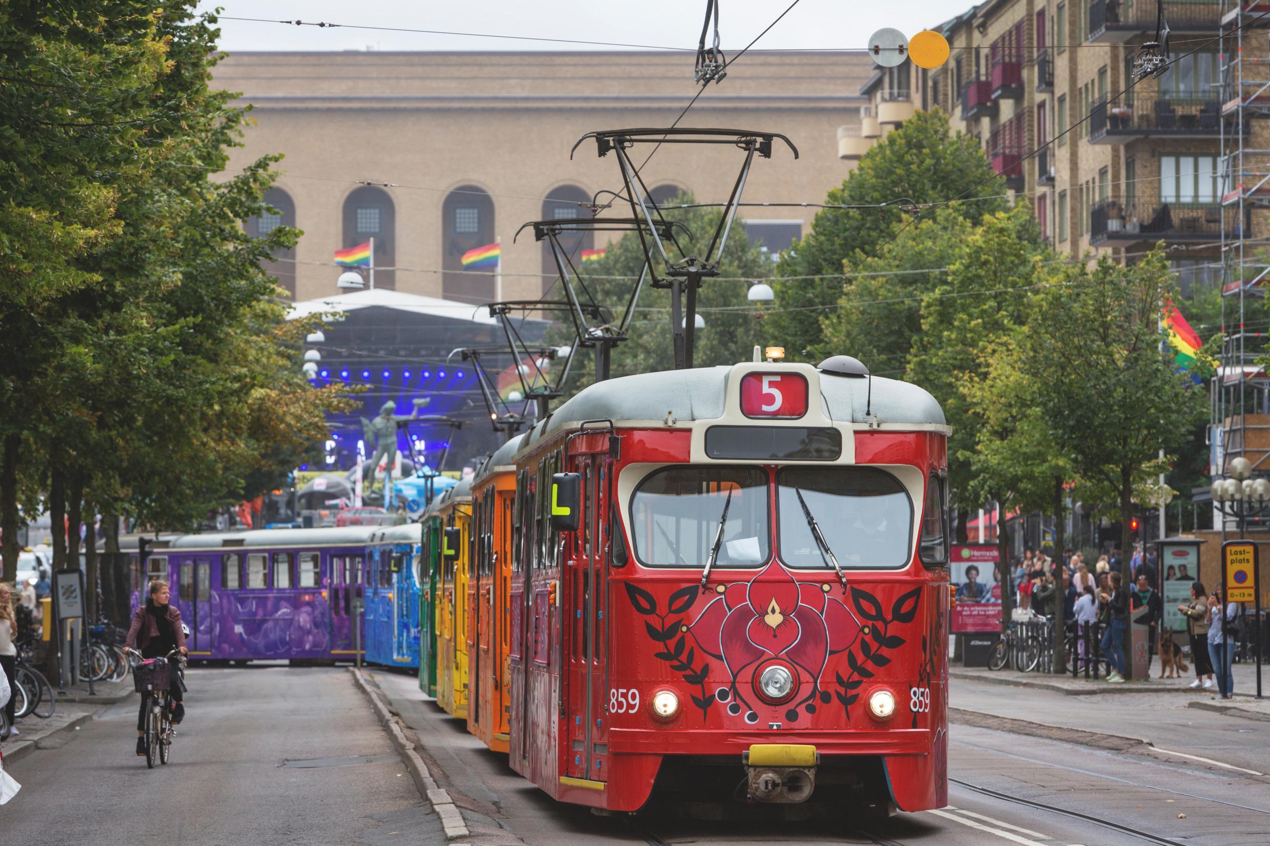 A tram going through a city is painted in colourful flowers, each car with one colour of the rainbow.