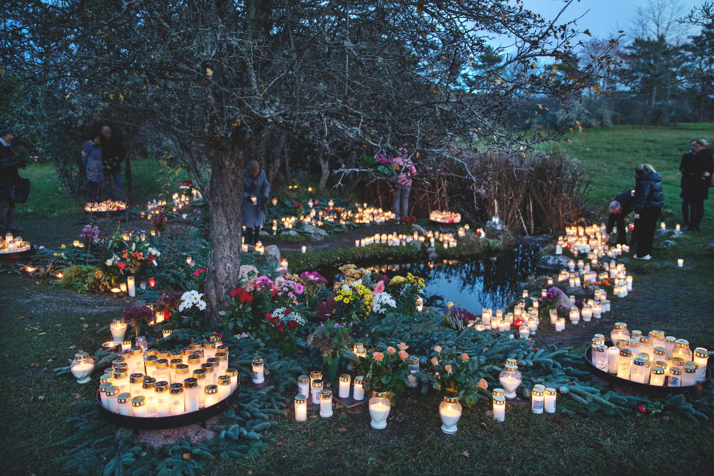 People stand at a cemetery surrounded by candles.