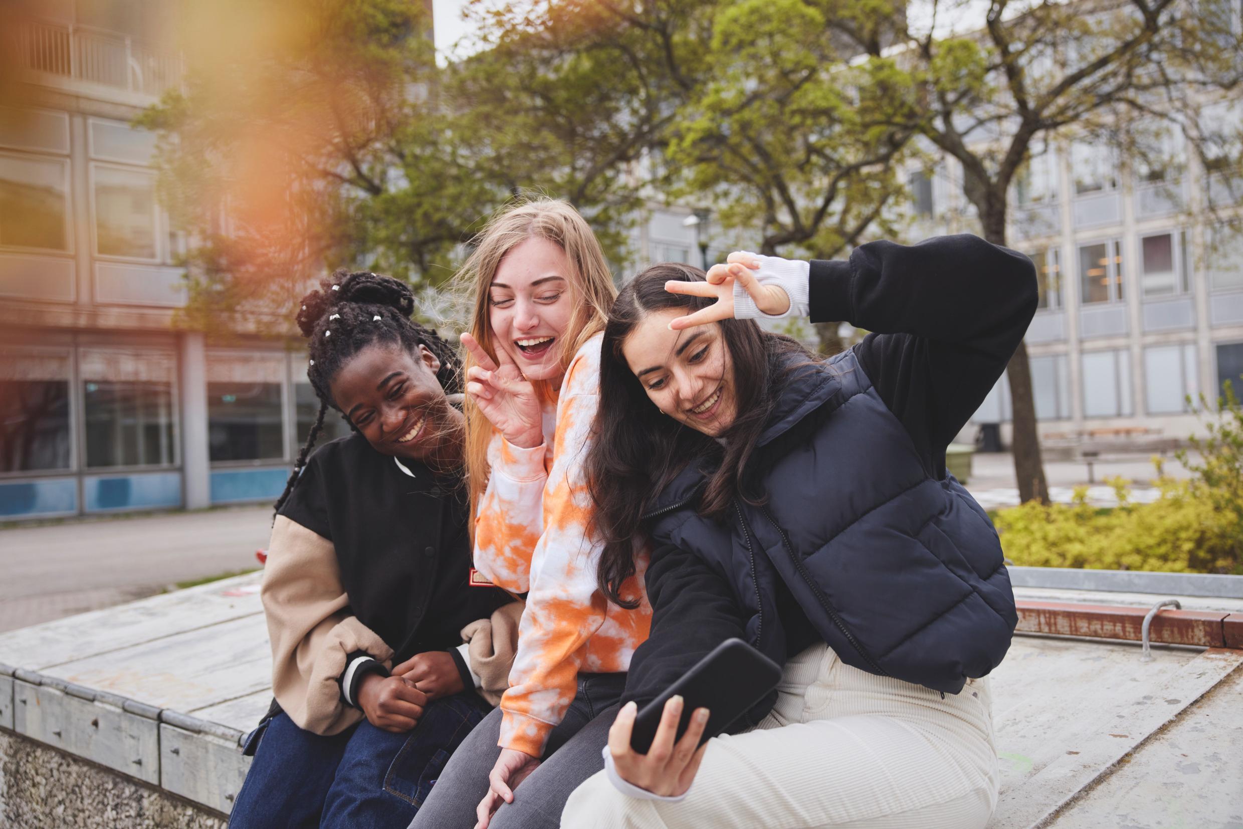 Teens sitting outside pose for a phone camera.