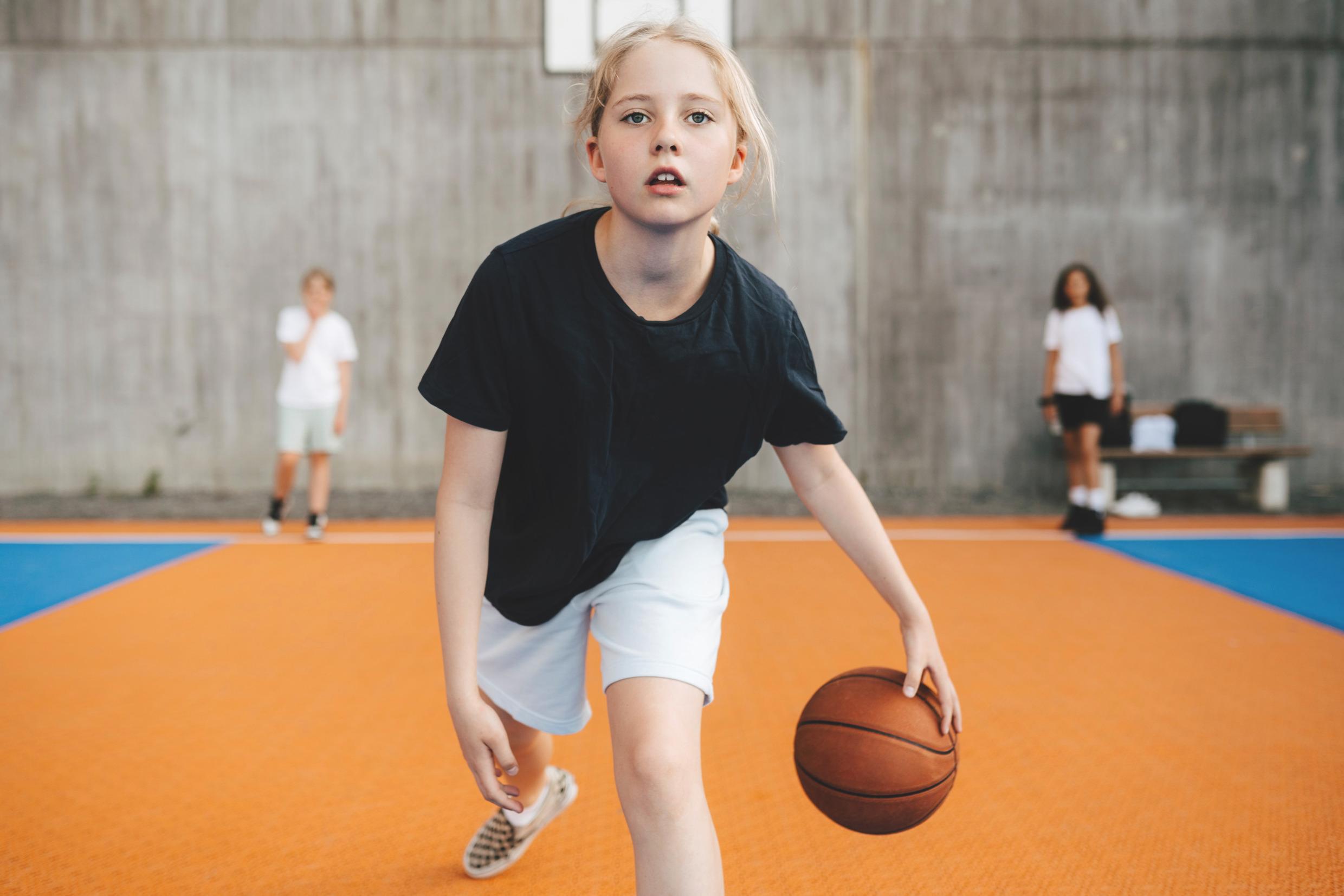 Kids practicing basketball indoors.