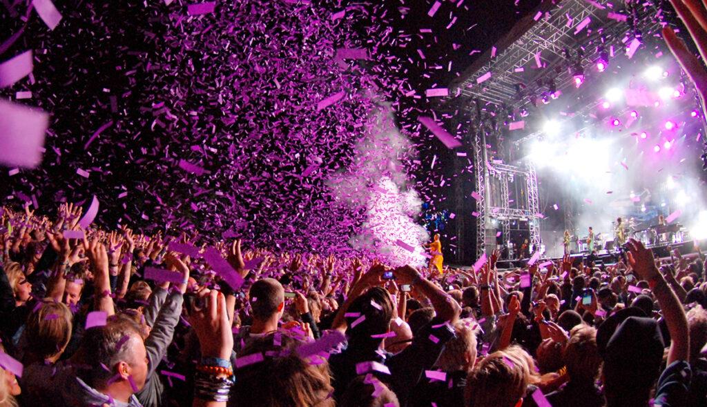 A big audience at a concert, with purple confetti in the air.