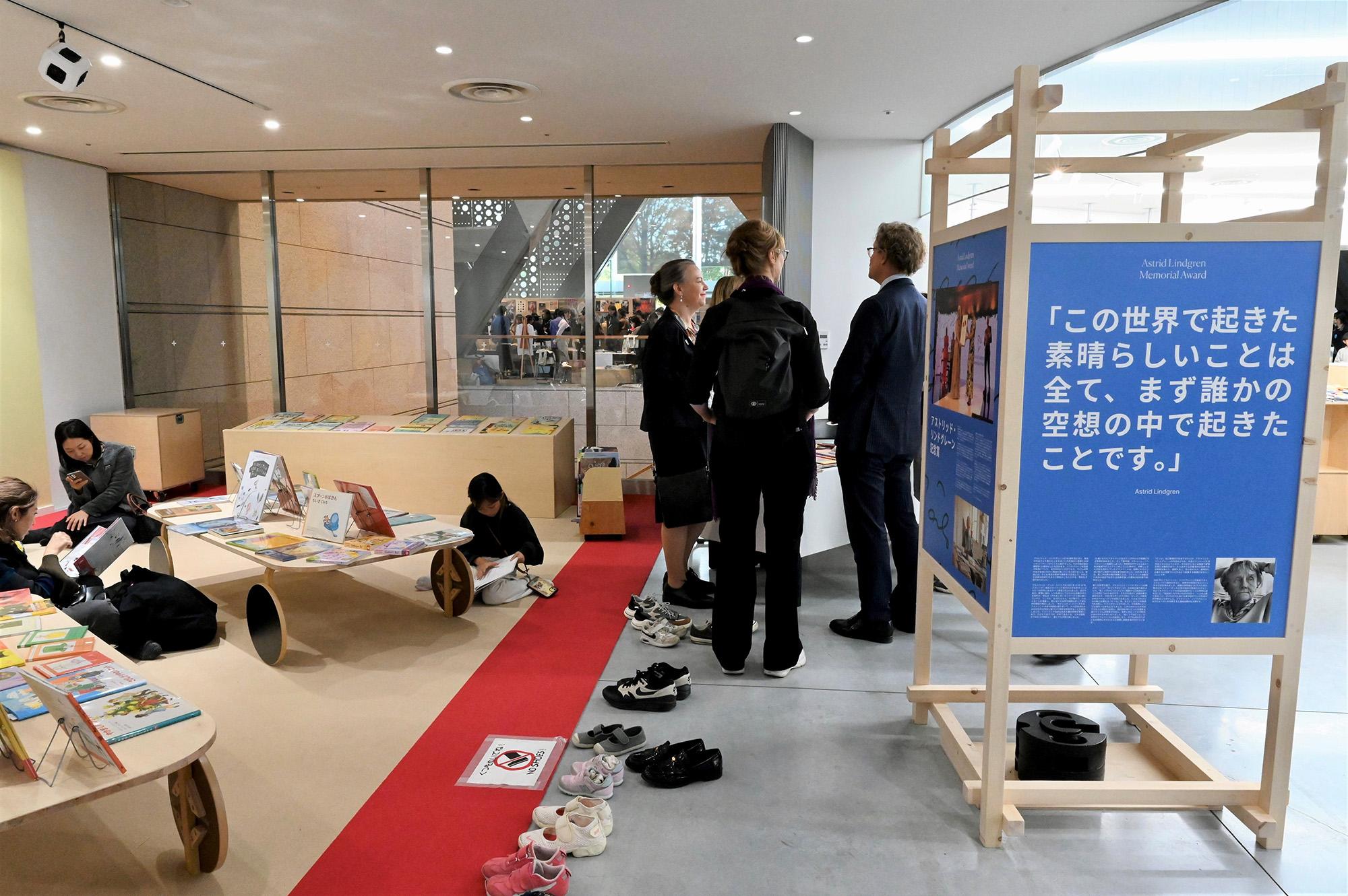 Children and adults reading books by the poster exhibition.