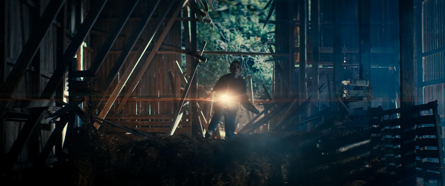 A young woman lights up a barn with a flashlight.