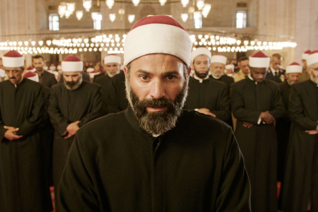 A man looking emotional with other men praying behind him. 