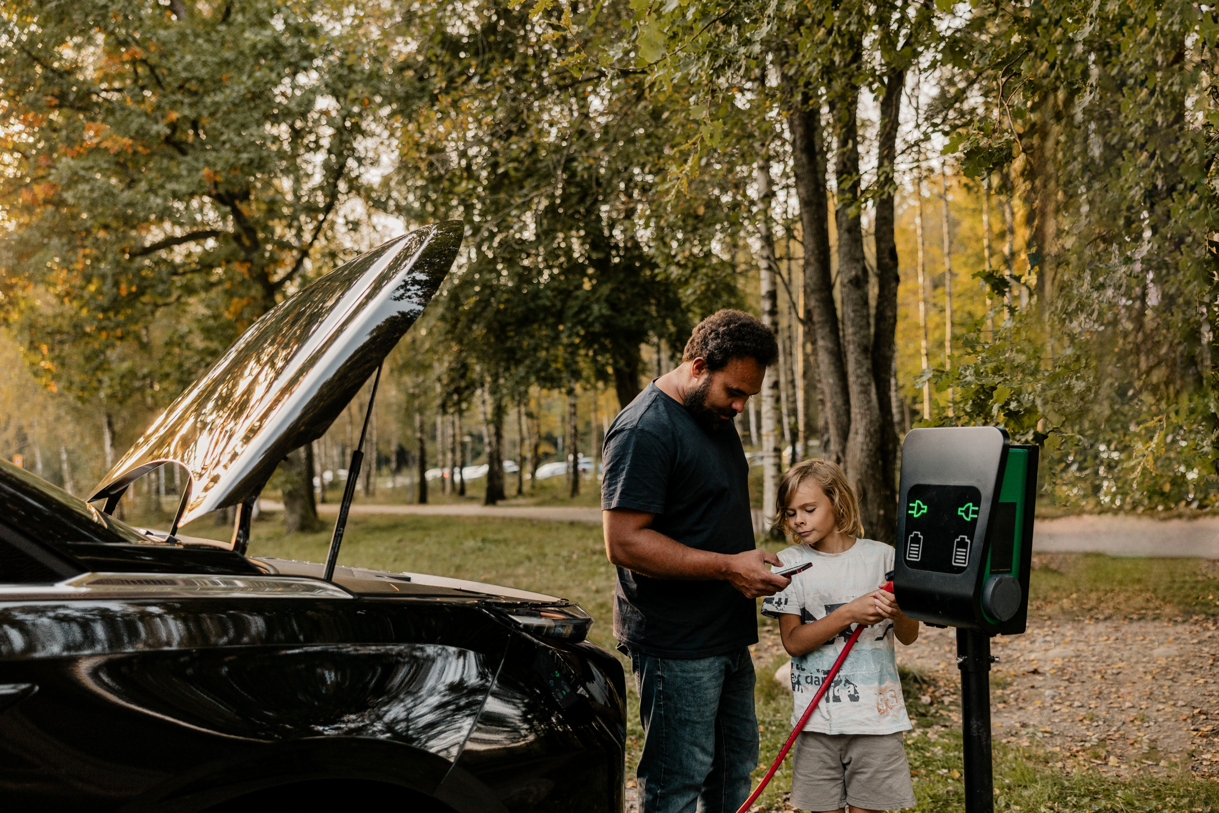 A man and a boy standing by a charging station in nature.